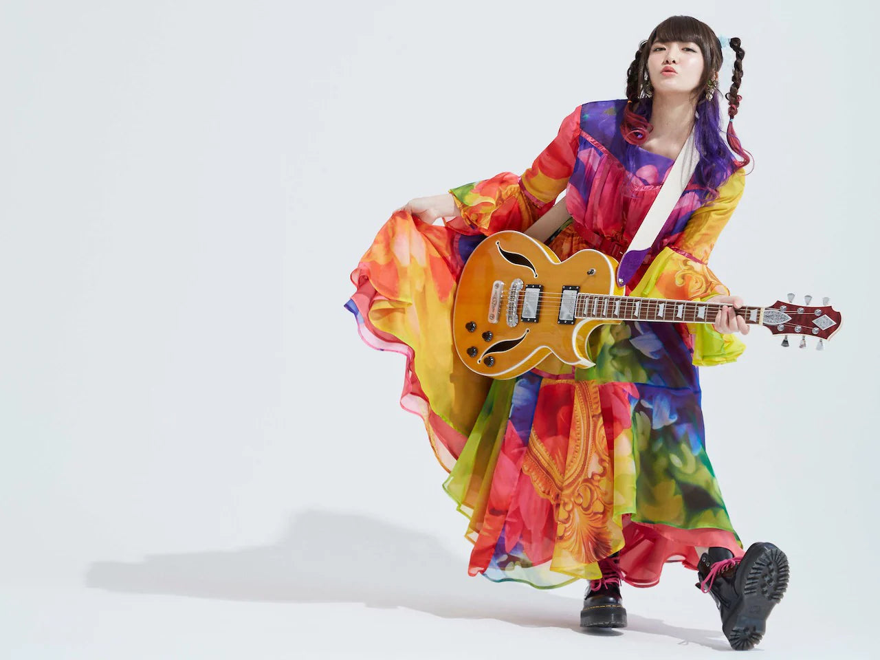 Miku Kobato in a colorful outfit playing a guitar on a white background